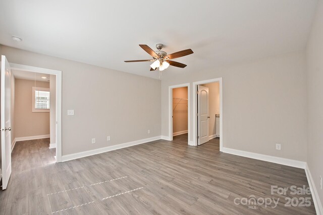 unfurnished bedroom with a closet, wood finished floors, baseboards, a walk in closet, and ceiling fan