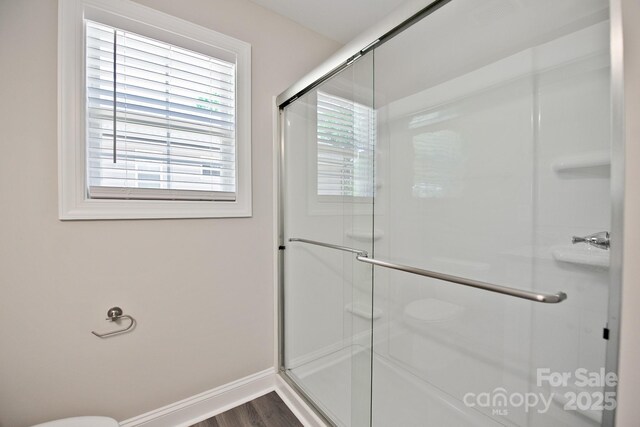bathroom featuring baseboards, wood finished floors, and a shower with shower door