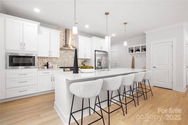 kitchen with ornamental molding, a kitchen island with sink, wall chimney exhaust hood, appliances with stainless steel finishes, and backsplash