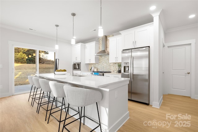 kitchen with decorative backsplash, stainless steel refrigerator with ice dispenser, crown molding, a spacious island, and wall chimney exhaust hood