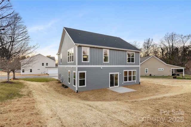 back of house with board and batten siding, roof with shingles, and dirt driveway