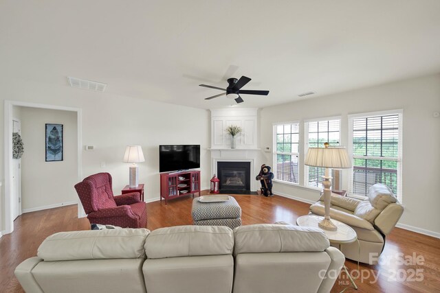 living area with ceiling fan, visible vents, a large fireplace, and wood finished floors