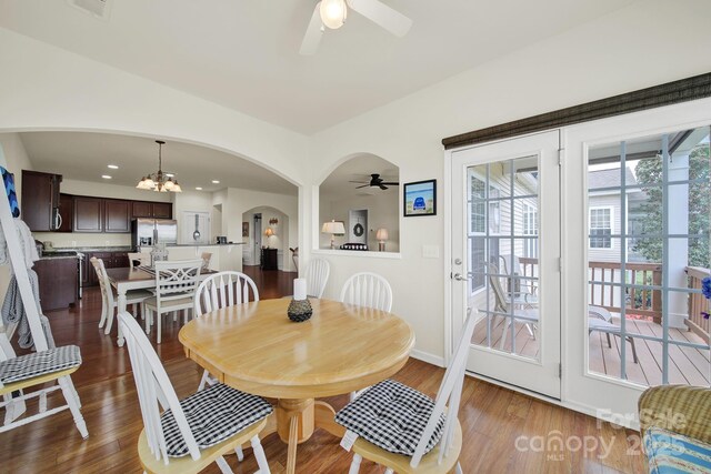 dining room featuring arched walkways, ceiling fan with notable chandelier, and wood finished floors