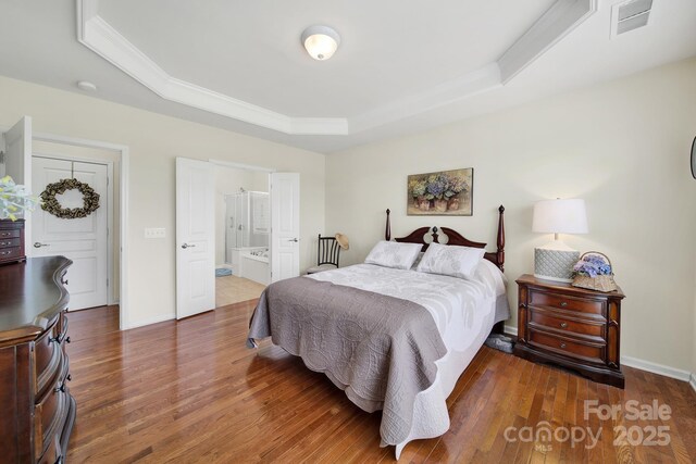 bedroom featuring baseboards, a tray ceiling, visible vents, and wood finished floors