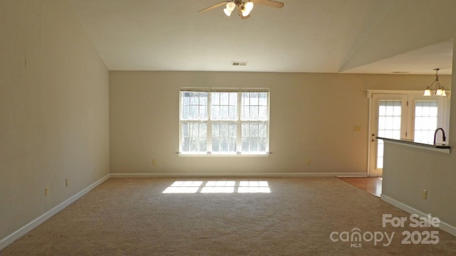 carpeted empty room featuring baseboards, ceiling fan with notable chandelier, and a healthy amount of sunlight