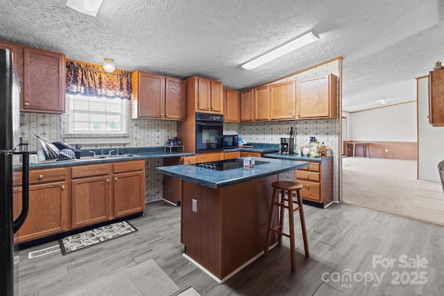 kitchen featuring dark countertops, a center island, black appliances, and light wood-style floors