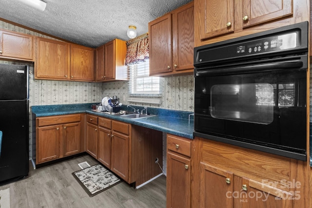 kitchen with brown cabinets, wallpapered walls, black appliances, and light wood-style floors