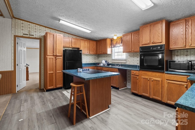 kitchen with dark countertops, brown cabinetry, wallpapered walls, a kitchen island, and black appliances