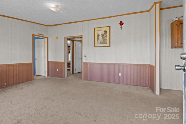 unfurnished room featuring visible vents, ornamental molding, a textured ceiling, a wainscoted wall, and carpet flooring