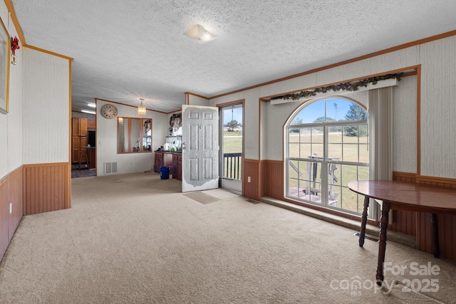 entryway featuring crown molding, a textured ceiling, wainscoting, and a wealth of natural light
