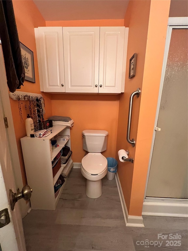 bathroom featuring baseboards, a shower stall, toilet, and wood finished floors