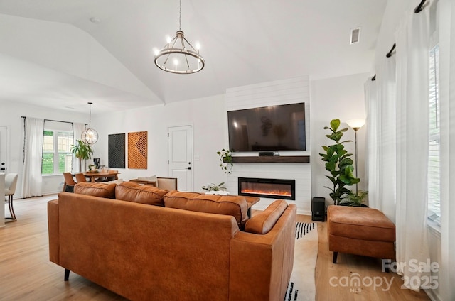 living room with a large fireplace, visible vents, light wood-type flooring, and a chandelier