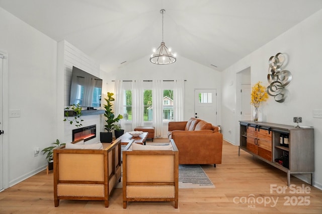 living area featuring light wood-style flooring, vaulted ceiling, a chandelier, and a fireplace