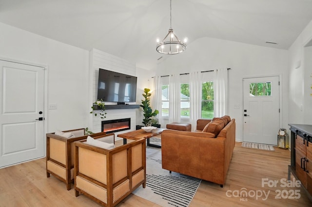 living room with a chandelier, high vaulted ceiling, a glass covered fireplace, and light wood-type flooring