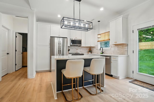 kitchen with backsplash, a kitchen island, appliances with stainless steel finishes, light countertops, and white cabinetry