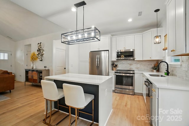 kitchen with a kitchen island, a sink, light wood-style flooring, appliances with stainless steel finishes, and backsplash