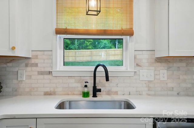 kitchen with light countertops, a sink, white cabinets, and tasteful backsplash