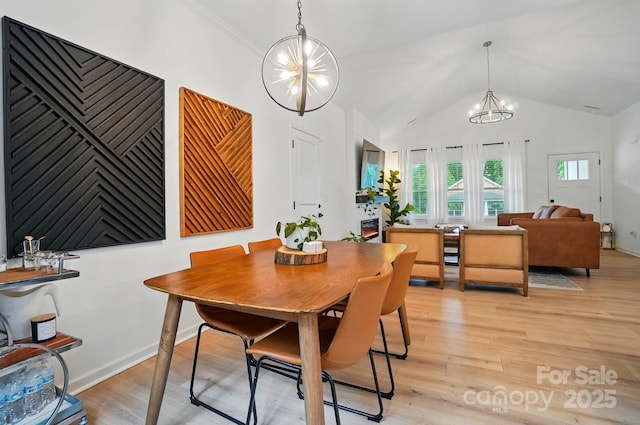 dining area with baseboards, a notable chandelier, lofted ceiling, and light wood finished floors