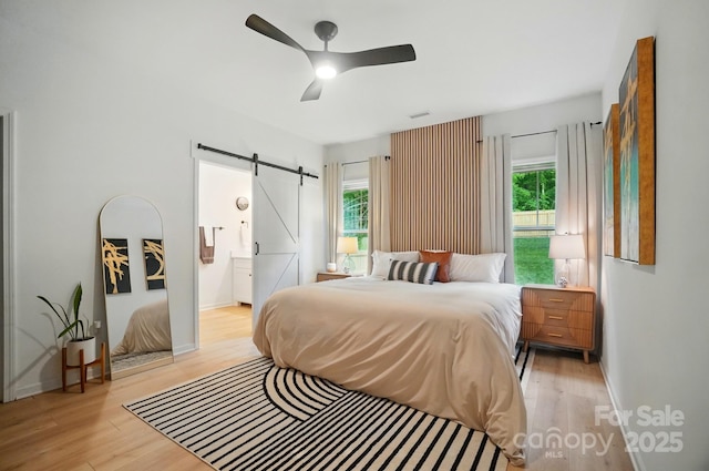 bedroom featuring multiple windows, light wood-type flooring, and a barn door