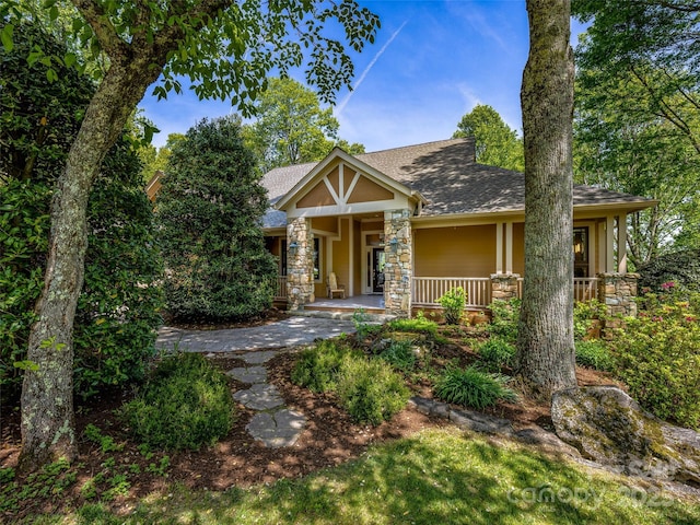 view of front facade with roof with shingles, stucco siding, covered porch, and stone siding