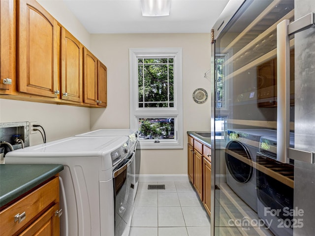 washroom featuring light tile patterned floors, baseboards, washing machine and dryer, and cabinet space