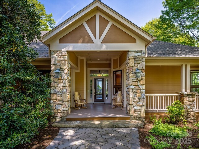 view of exterior entry featuring a shingled roof, covered porch, and stone siding