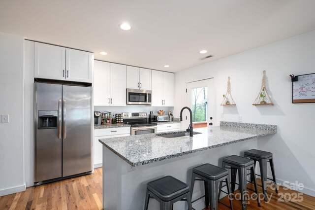 kitchen featuring a kitchen bar, appliances with stainless steel finishes, a sink, white cabinets, and a peninsula