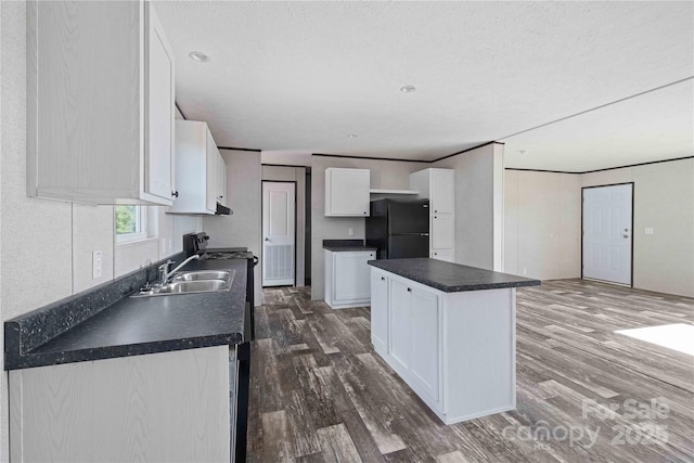 kitchen featuring dark countertops, a center island, dark wood finished floors, freestanding refrigerator, and white cabinetry