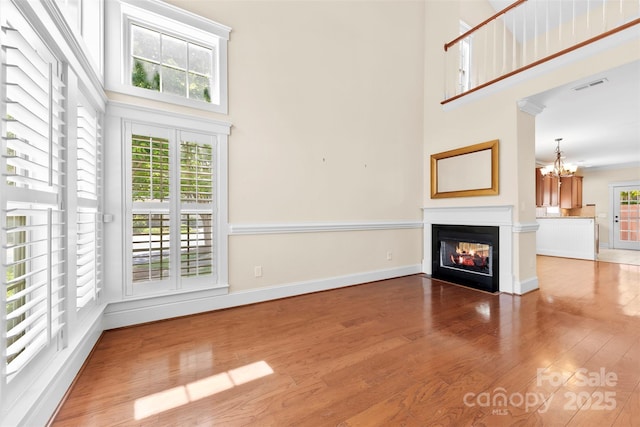 unfurnished living room featuring a chandelier, a glass covered fireplace, wood finished floors, a towering ceiling, and visible vents