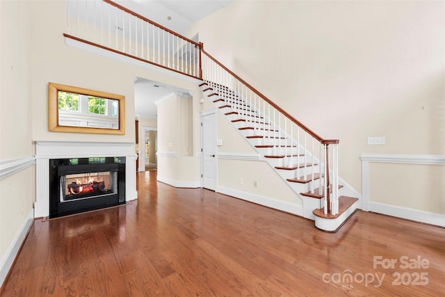 unfurnished living room with a multi sided fireplace, a towering ceiling, wood finished floors, stairway, and baseboards