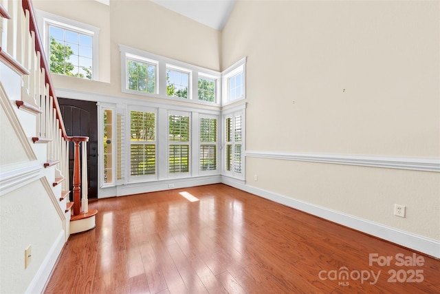 unfurnished living room featuring a towering ceiling, a healthy amount of sunlight, stairway, and wood finished floors