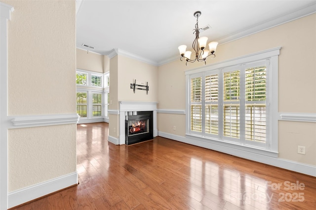 unfurnished living room featuring visible vents, crown molding, wood finished floors, a chandelier, and a glass covered fireplace