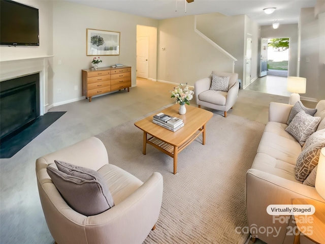 living area with light colored carpet, a glass covered fireplace, stairs, a ceiling fan, and baseboards