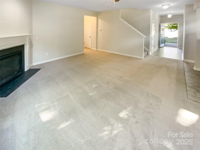 unfurnished living room with ceiling fan, a fireplace, carpet floors, baseboards, and stairway