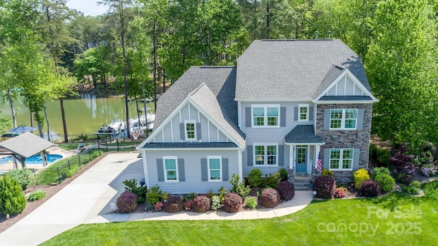 view of front of property featuring a front lawn, fence, stone siding, a shingled roof, and a water view