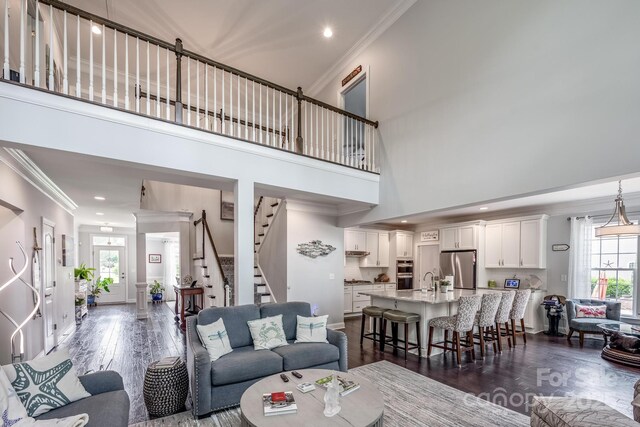 living area featuring crown molding, dark wood-style flooring, a towering ceiling, and stairs