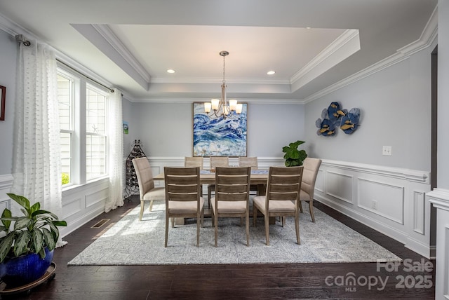 dining area featuring a tray ceiling, visible vents, wood finished floors, a notable chandelier, and a decorative wall