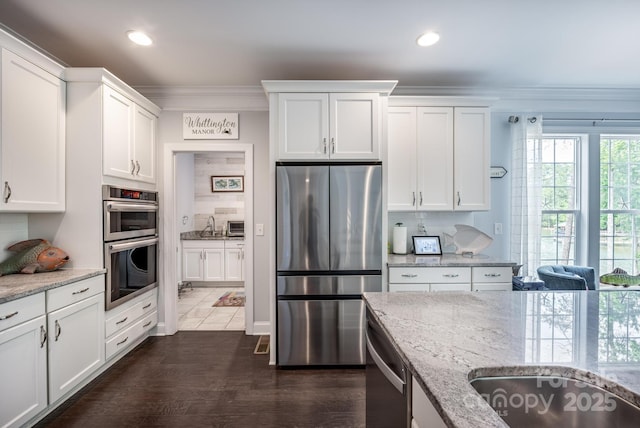 kitchen with white cabinets, light stone counters, stainless steel appliances, decorative backsplash, and ornamental molding