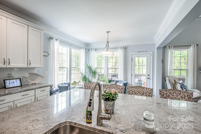 kitchen with decorative backsplash, crown molding, hanging light fixtures, light stone counters, and white cabinets
