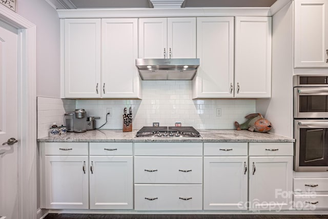 kitchen with tasteful backsplash, light stone counters, under cabinet range hood, stainless steel appliances, and white cabinetry