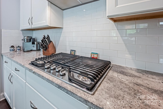 kitchen featuring white cabinets, light stone counters, stainless steel gas stovetop, and tasteful backsplash