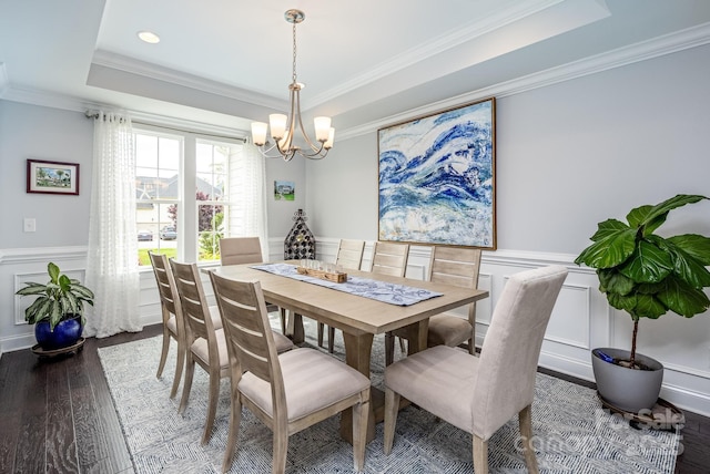 dining room featuring wainscoting, wood finished floors, a raised ceiling, an inviting chandelier, and ornamental molding