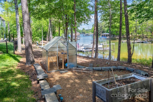 view of yard featuring a boat dock, a water view, an outdoor structure, and a greenhouse