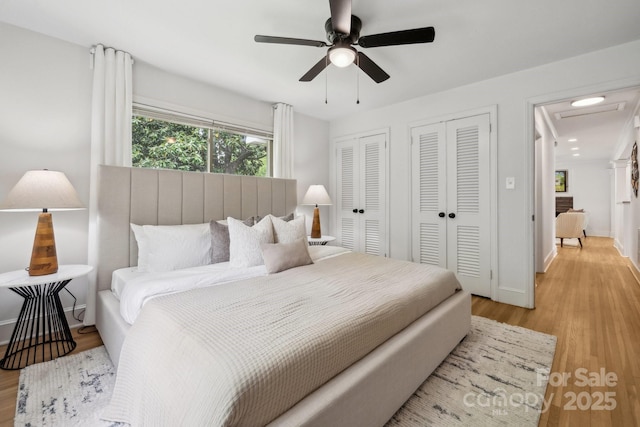 bedroom with a ceiling fan, baseboards, multiple closets, and light wood-type flooring
