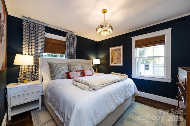 bedroom featuring baseboards, wood finished floors, ornamental molding, and a chandelier