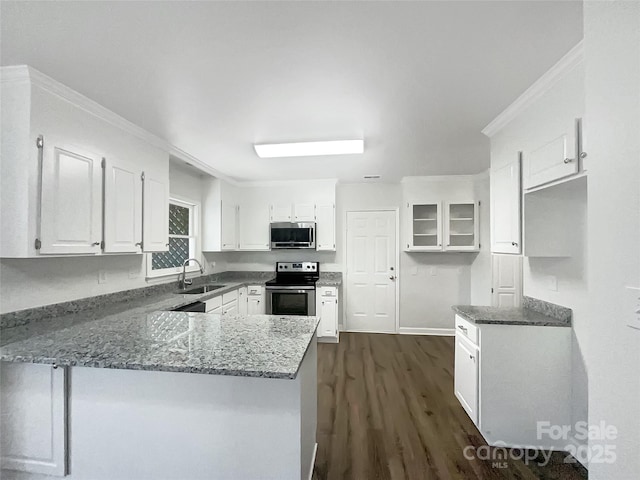 kitchen featuring white cabinets, a sink, dark stone countertops, stainless steel appliances, and a peninsula