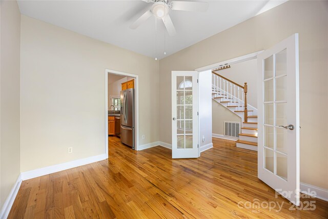 empty room with french doors, light wood-style floors, stairway, baseboards, and a ceiling fan