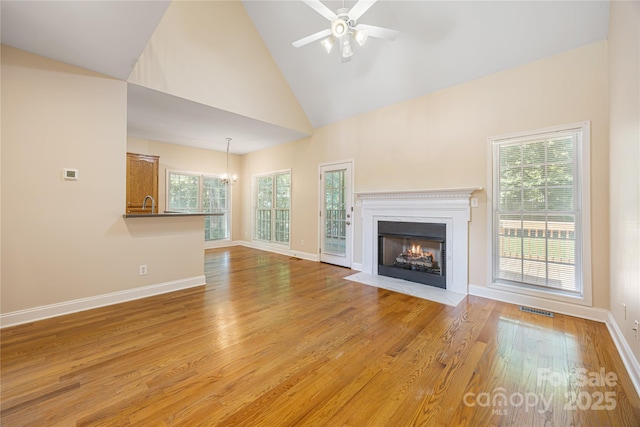unfurnished living room with a chandelier, a fireplace with flush hearth, a ceiling fan, healthy amount of natural light, and high vaulted ceiling