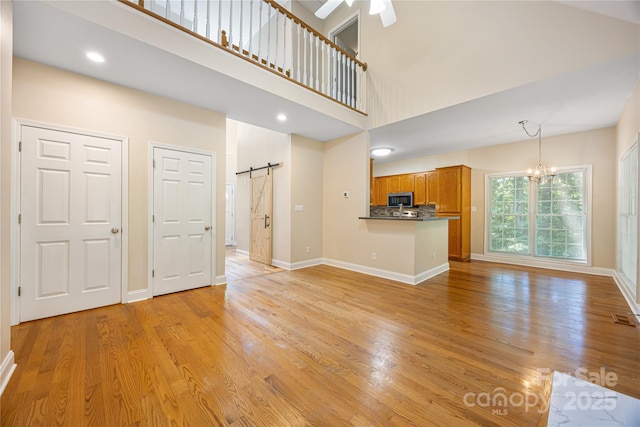 unfurnished living room featuring a barn door, a chandelier, a high ceiling, light wood finished floors, and baseboards