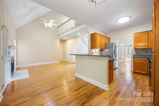 kitchen featuring a ceiling fan, light wood-style floors, dark countertops, stainless steel fridge, and a peninsula